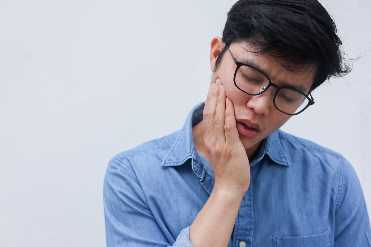close up young asian man frown and use hand to massage on cheek after feeling pain or hurt from tmj muscle symptom at home for un healthy lifestyle and treatment concept