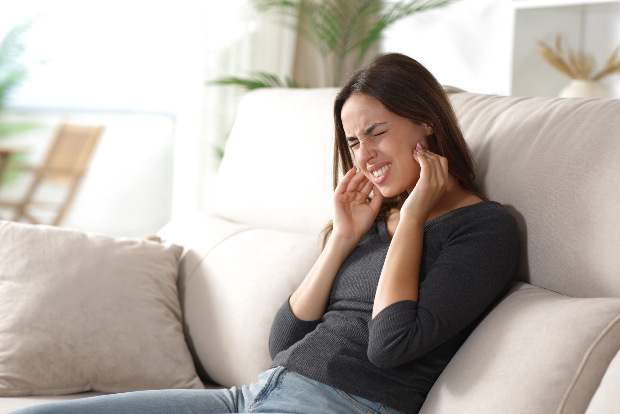 Stressed woman suffering jaw ache and complaining sitting on a sofa at home