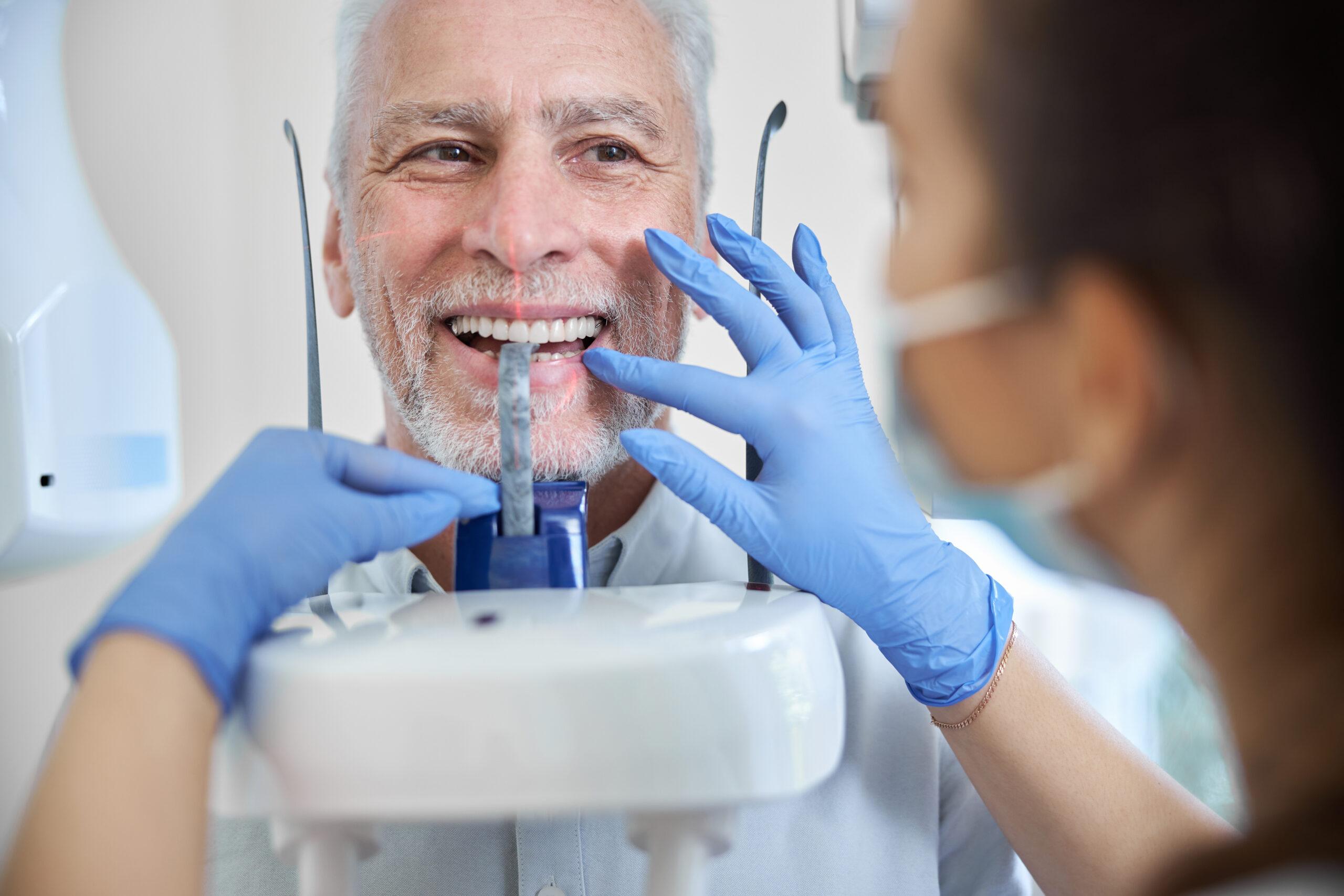 Close-up photo of a skillful dental technician preparing a senior man for a panoramic dental x-ray