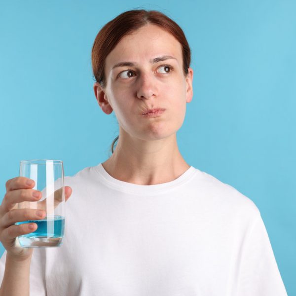 Woman rinsing mouth with mouthwash on light blue background