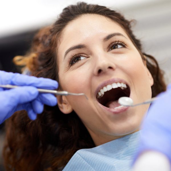 Head and shoulders portrait of beautiful young woman lying in dental chair with mouth open during consultation, copy space