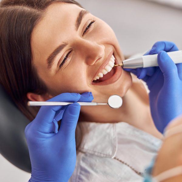Female patient at dental procedure, doctor using dental instruments in modern dental clinic.